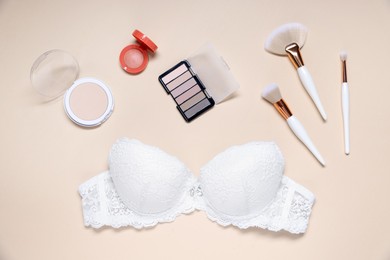 Photo of Flat lay composition with white lace bra and cosmetic products on beige background