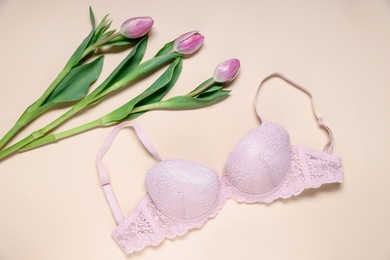 Photo of Pink lace bra and tulip flowers on beige background, flat lay