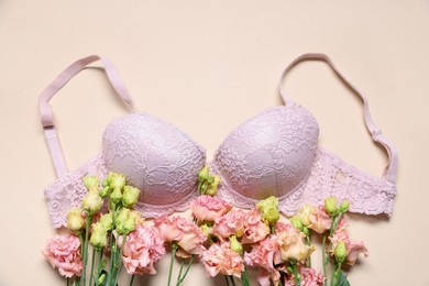 Photo of Pink lace bra and eustoma flowers on beige background, flat lay