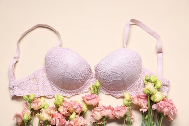 Photo of Pink lace bra and eustoma flowers on beige background, flat lay
