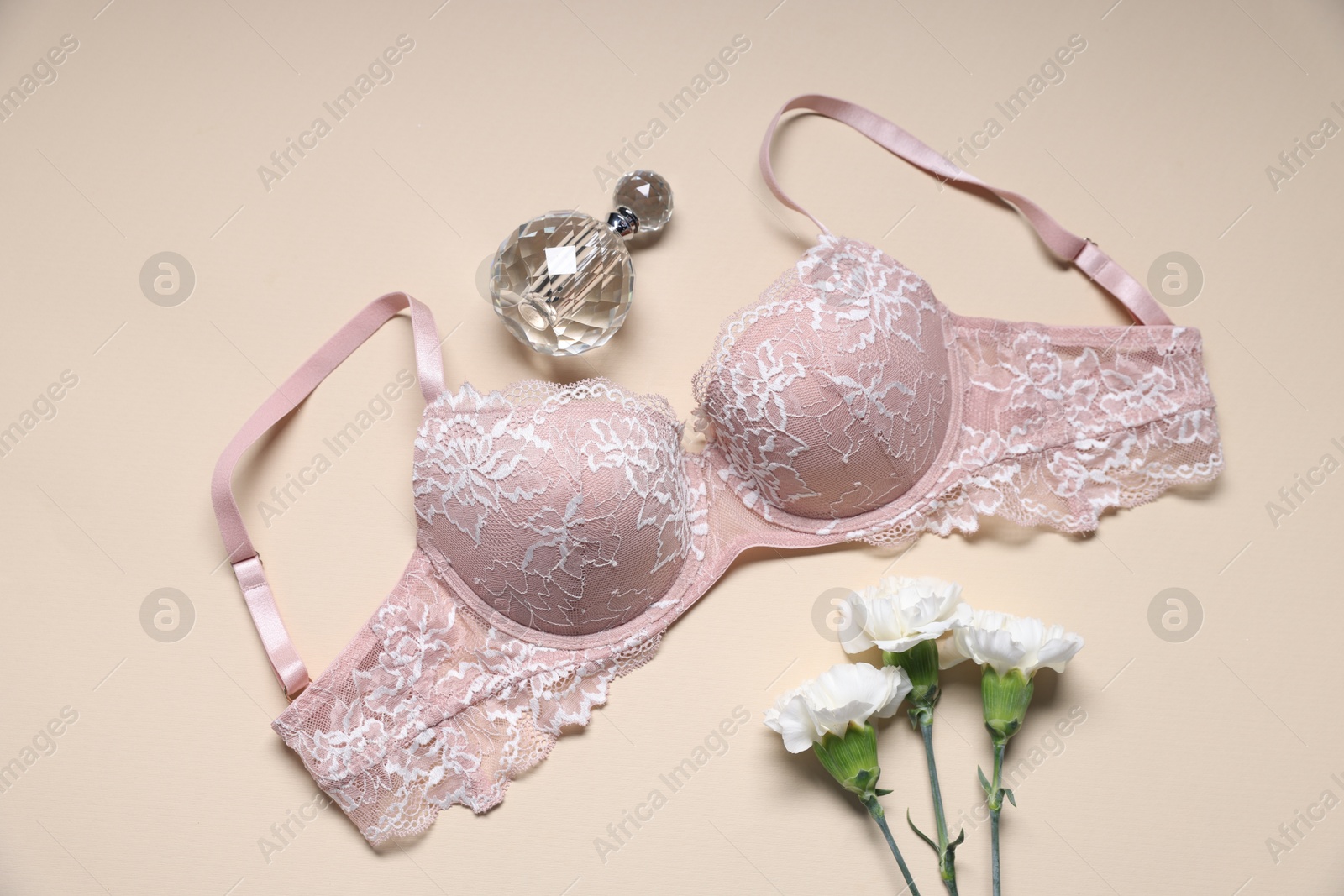 Photo of Pink lace bra, perfume and flowers on beige background, flat lay