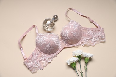 Photo of Pink lace bra, perfume and flowers on beige background, flat lay