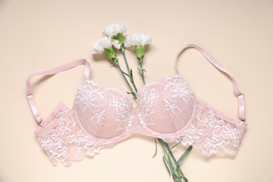 Photo of Pink lace bra and flowers on beige background, top view