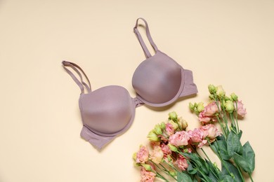 Photo of Beautiful bra and eustoma flowers on beige background, flat lay