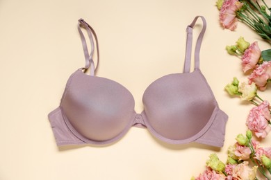 Photo of Beautiful bra and eustoma flowers on beige background, flat lay