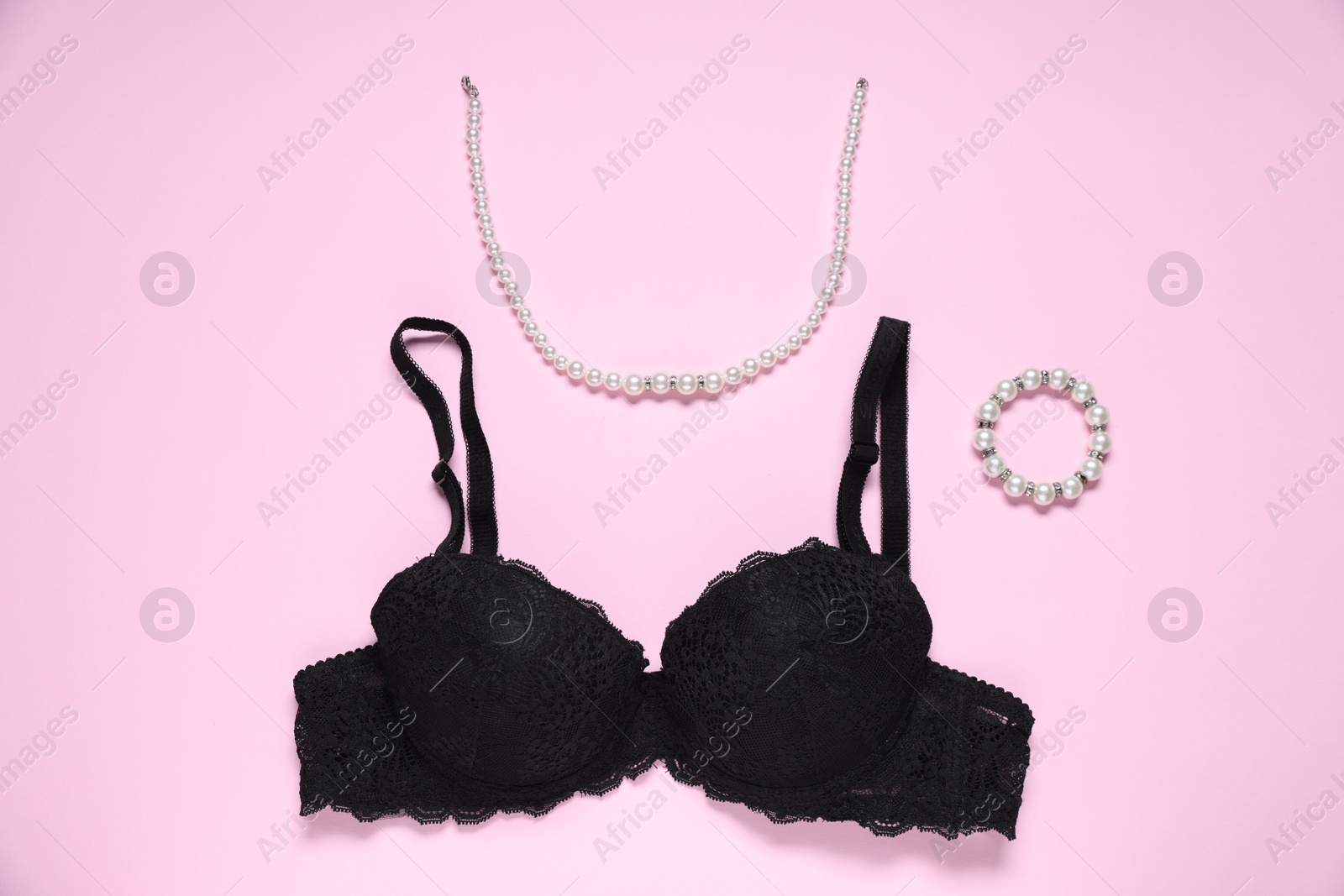 Photo of Black lace bra and jewelry on pink background, flat lay