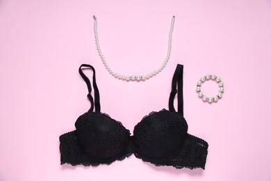 Photo of Black lace bra and jewelry on pink background, flat lay