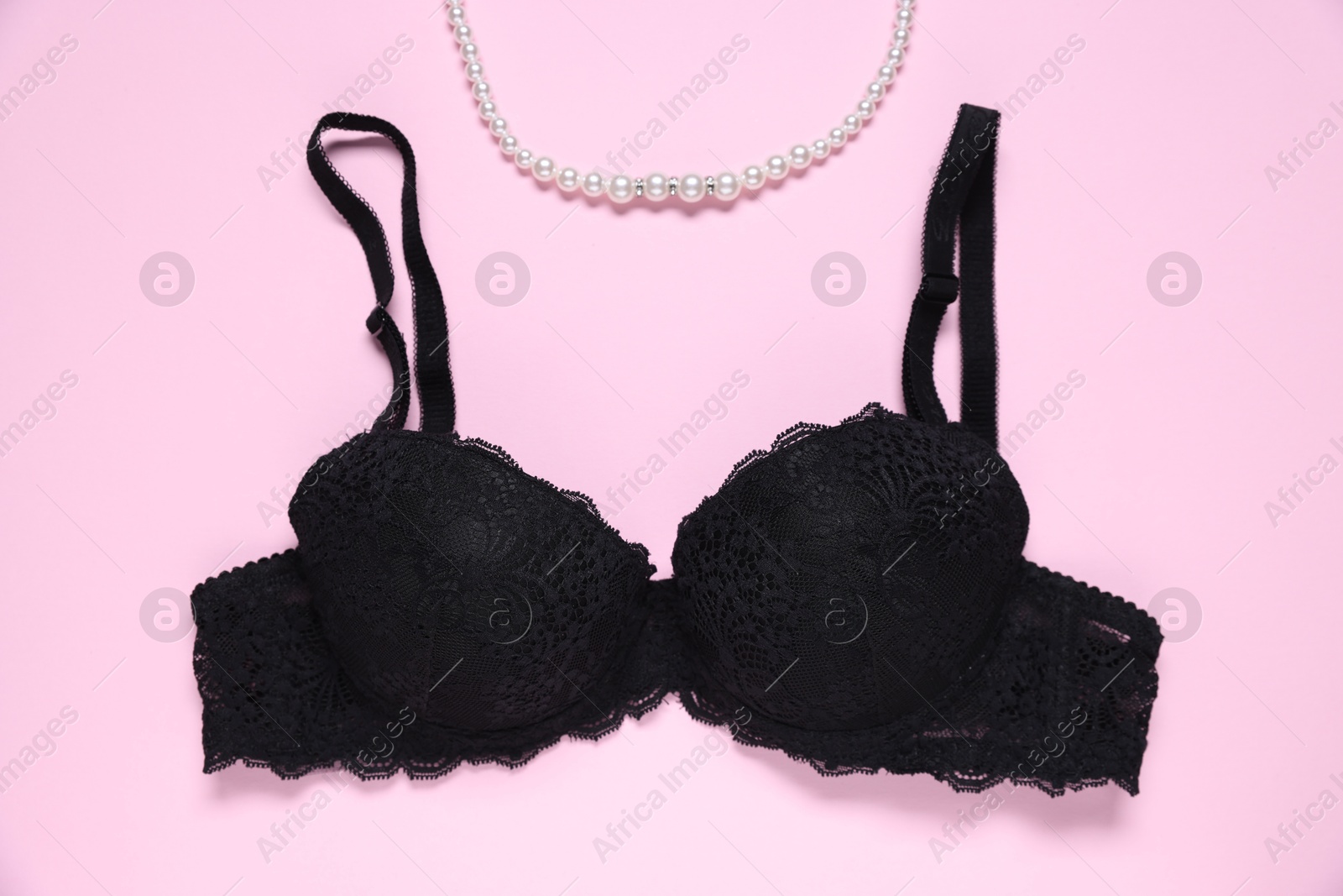 Photo of Black lace bra and necklace on pink background, flat lay