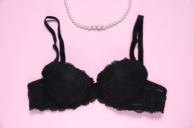 Photo of Black lace bra and necklace on pink background, flat lay