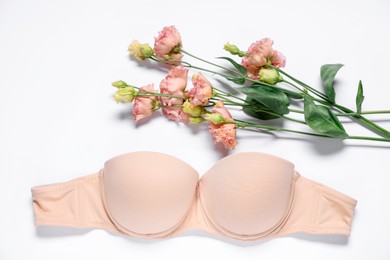 Photo of Beige bra and eustoma flowers on white background, flat lay