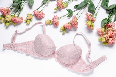 Photo of Pink lace bra and eustoma flowers on white background, flat lay