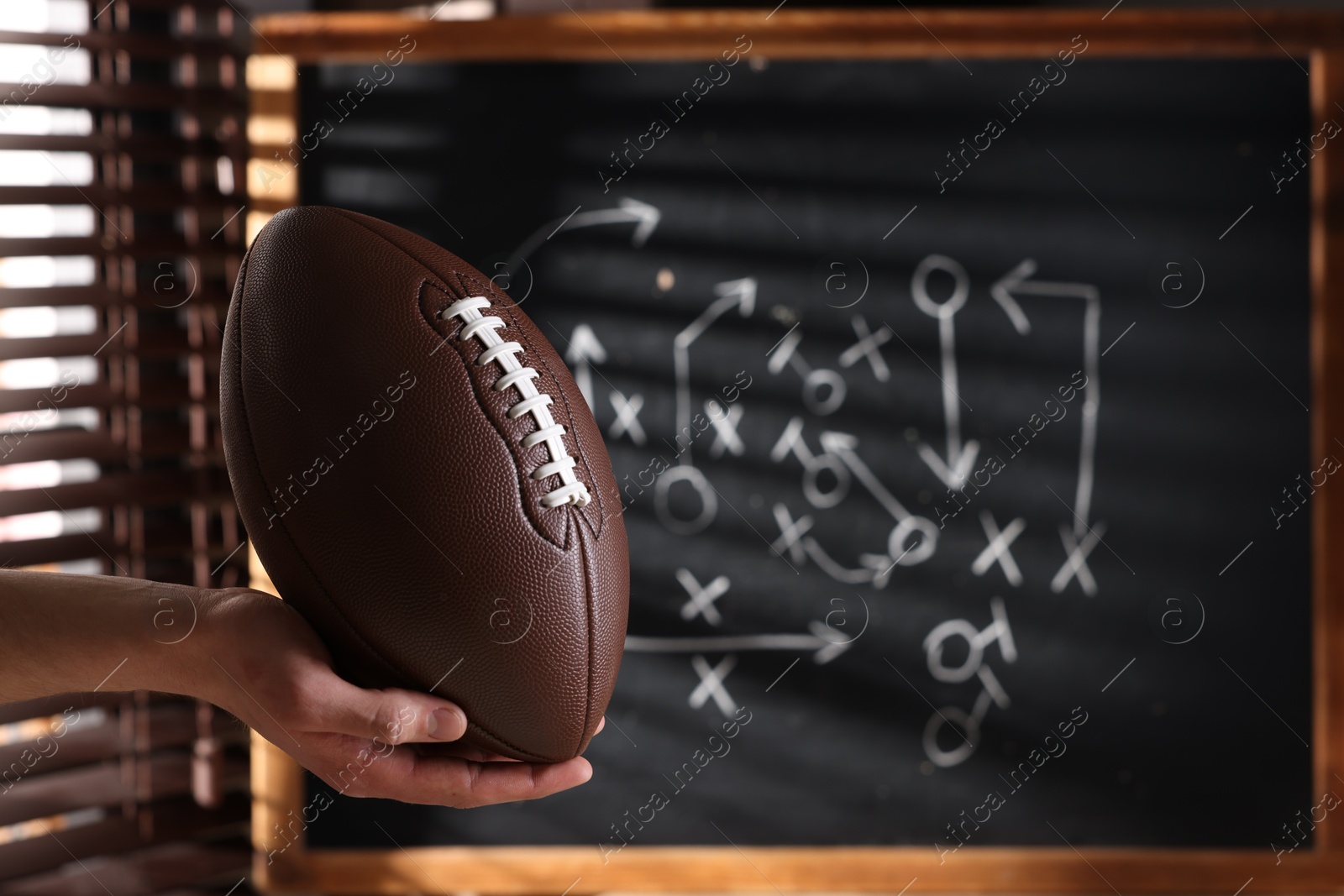 Man holding American football ball near chalkboard with scheme of game, closeup Photo of Man holding American football ball near chalkboard with scheme of game, closeup