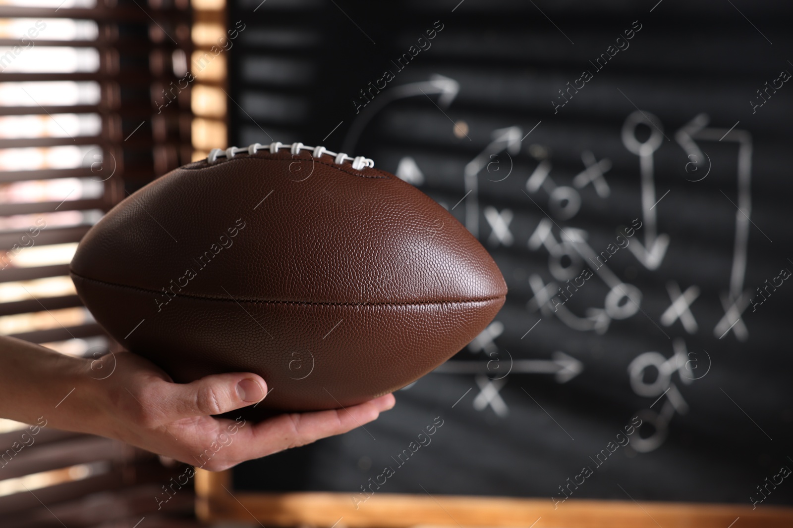 Man holding American football ball near chalkboard with scheme of game, closeup Photo of Man holding American football ball near chalkboard with scheme of game, closeup