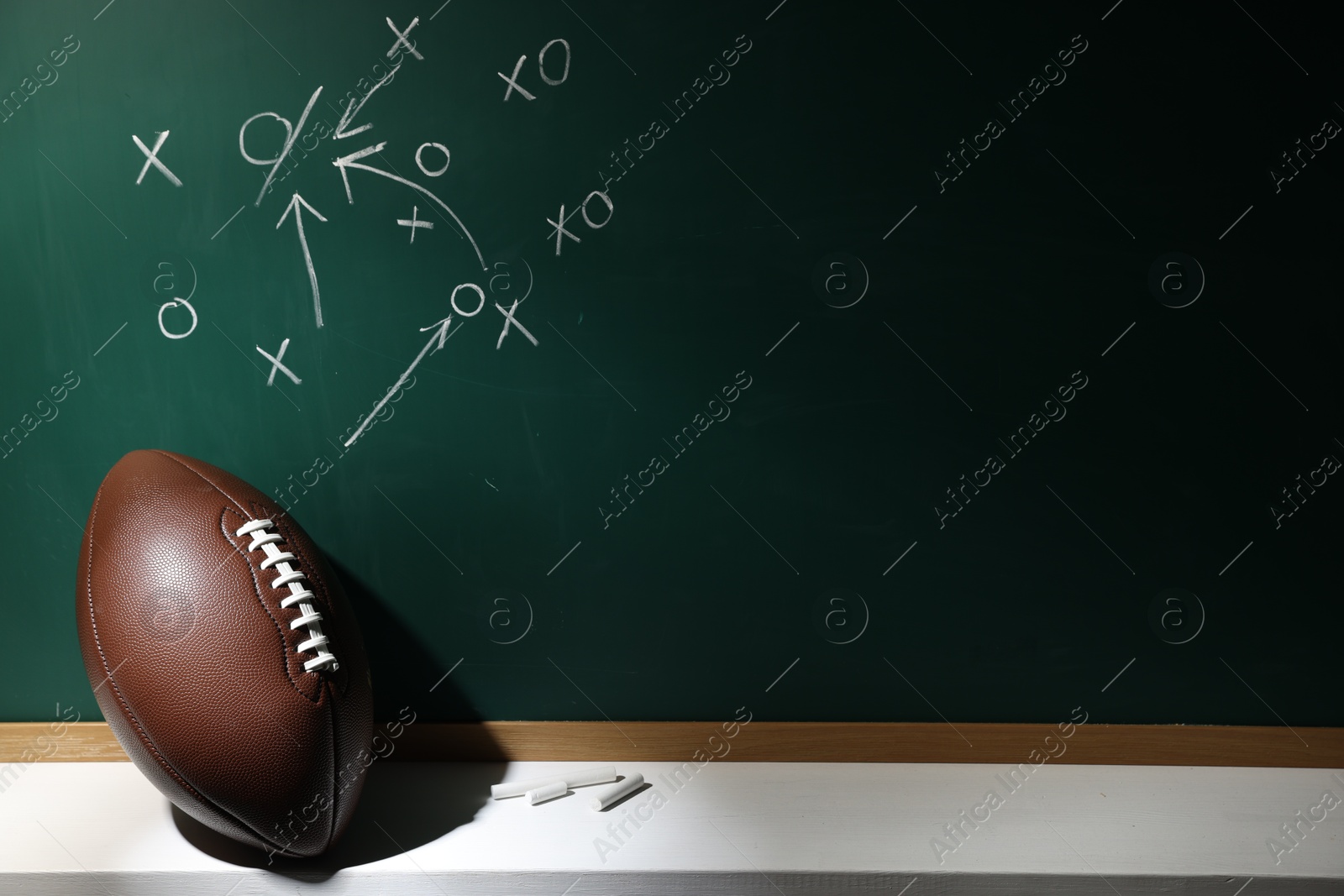 American football ball and pieces of chalk near chalkboard with game scheme, space for text Photo of American football ball and pieces of chalk near chalkboard with game scheme, space for text