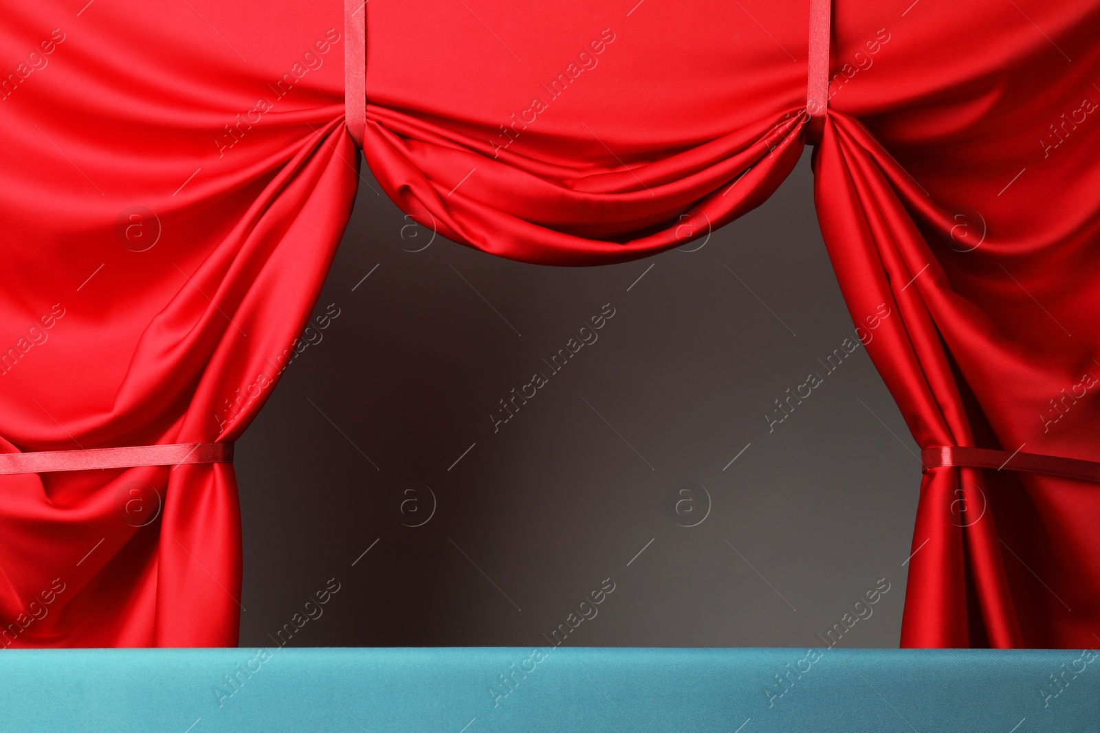 Puppet show. Empty light blue stage with red curtains against grey background Photo of Puppet show. Empty light blue stage with red curtains against grey background