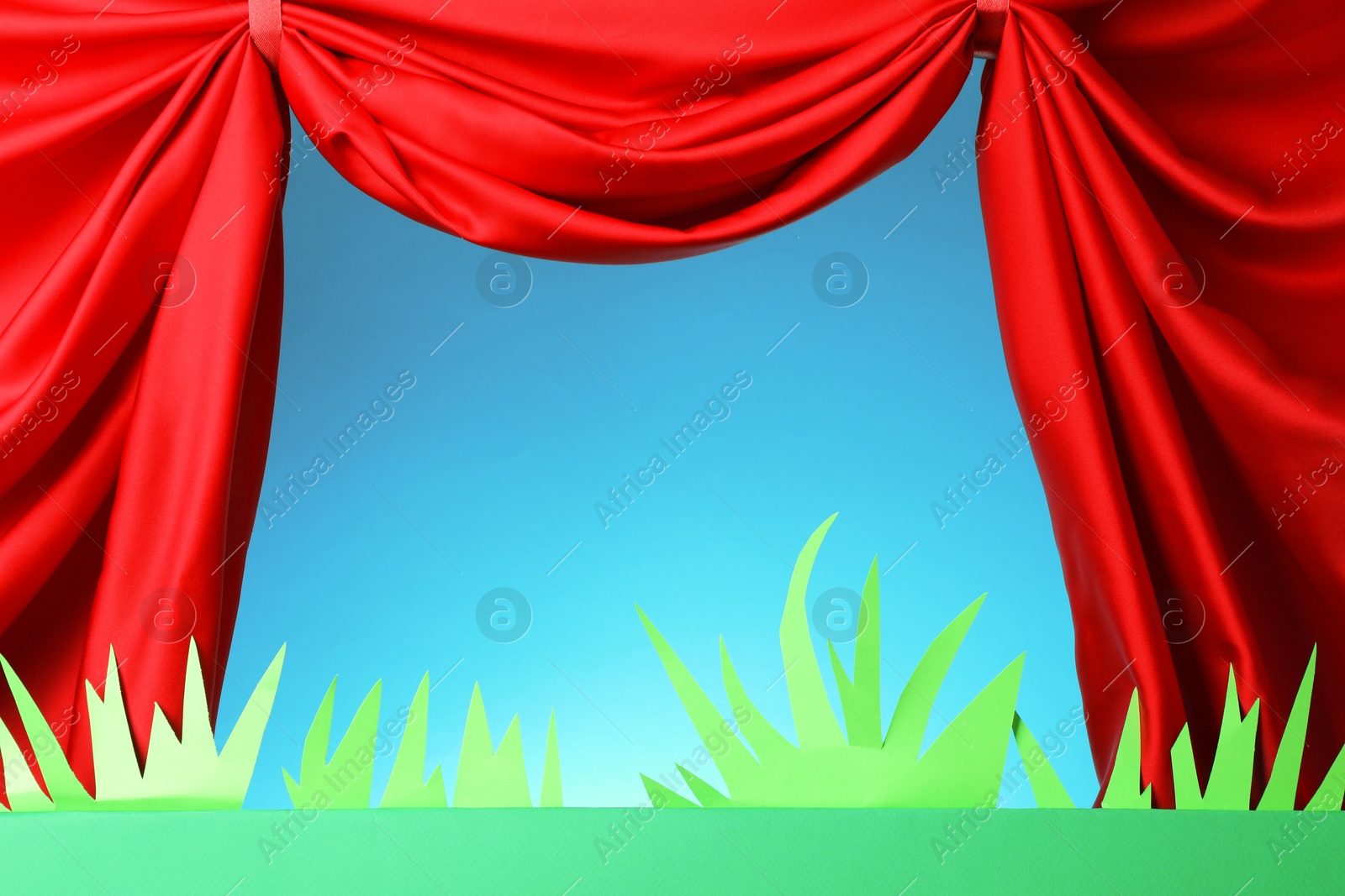 Photo of Puppet show. Empty green stage with decorations and red curtains against light blue background