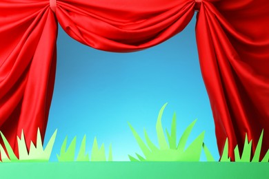 Photo of Puppet show. Empty green stage with decorations and red curtains against light blue background