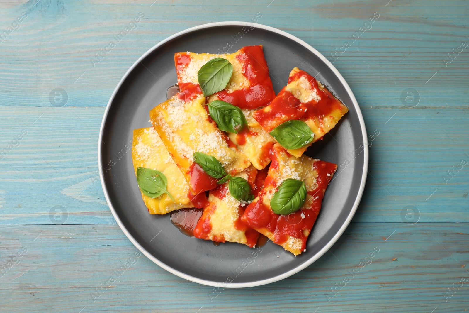 Delicious ravioli with tomato sauce, parmesan cheese and basil on blue wooden table, top view Photo of Delicious ravioli with tomato sauce, parmesan cheese and basil on blue wooden table, top view