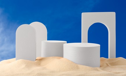 Image of White podiums and figures in sand against blue sky, banner design