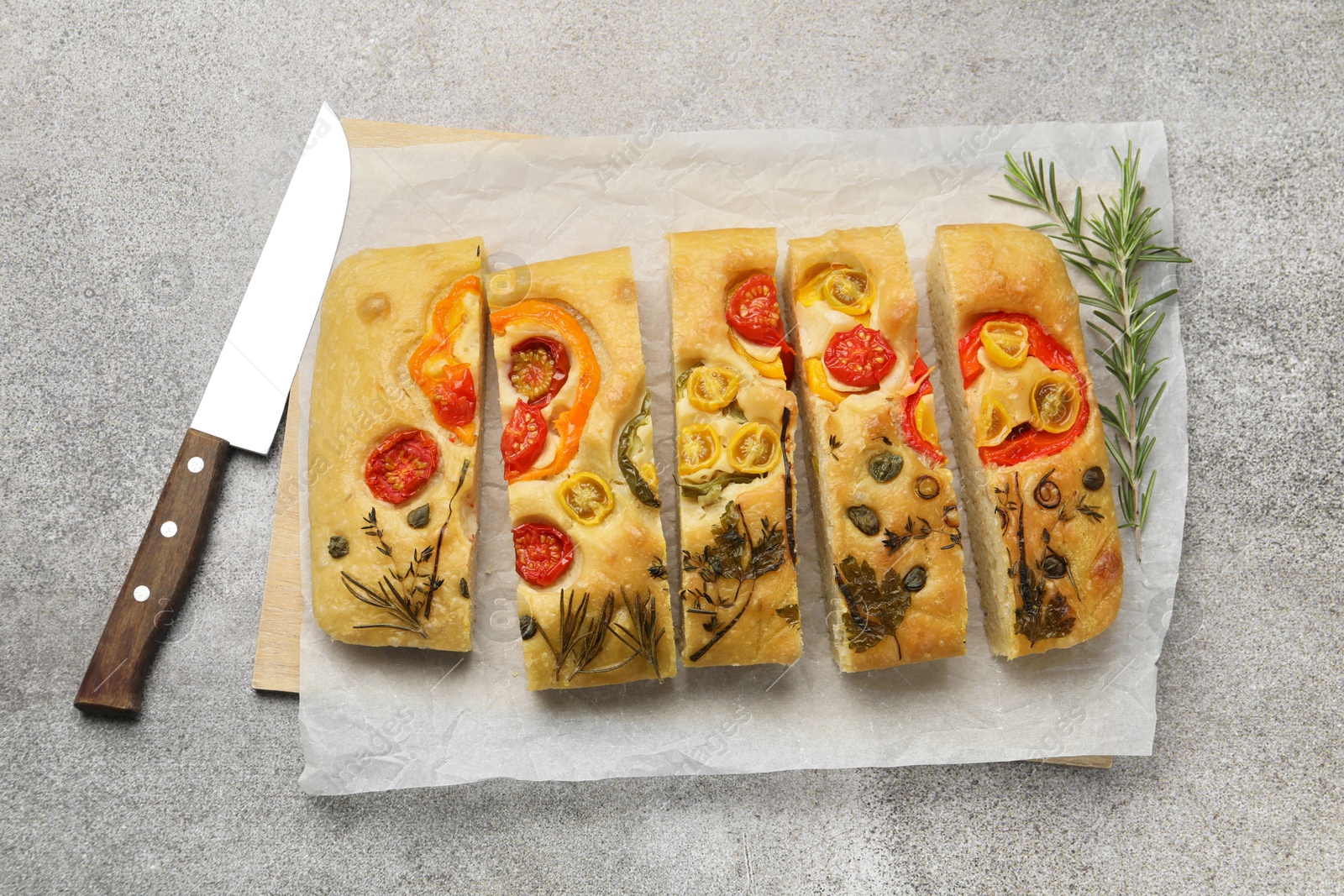 Cut delicious focaccia with flowers made of vegetables, knife and rosemary on grey table, top view Photo of Cut delicious focaccia with flowers made of vegetables, knife and rosemary on grey table, top view