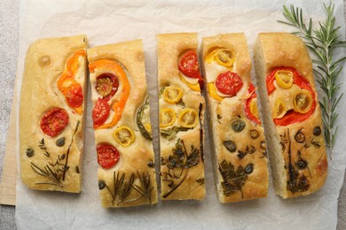 Photo of Cut delicious focaccia with flowers made of vegetables and rosemary on grey table, top view