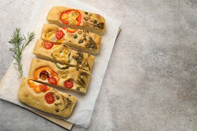 Photo of Cut delicious focaccia with flowers made of vegetables and rosemary on grey table, top view. Space for text