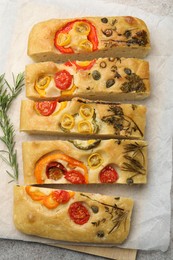Photo of Cut delicious focaccia with flowers made of vegetables and rosemary on grey table, top view