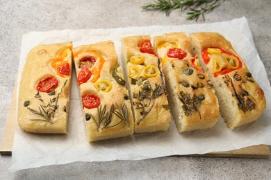Photo of Cut delicious focaccia with flowers made of vegetables on grey table, closeup