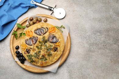 Photo of Delicious focaccia with flowers made of vegetables and cutter on grey table, top view. Space for text