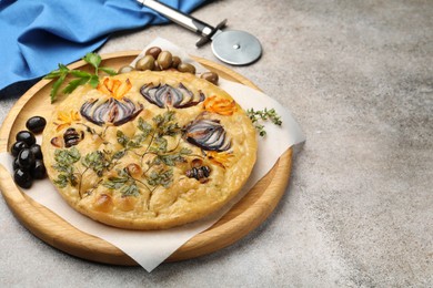Photo of Delicious focaccia with flowers made of vegetables and cutter on grey table, closeup. Space for text
