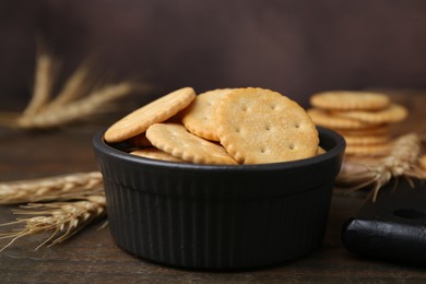 Photo of Tasty salty crackers and wheat spikes on wooden table, closeup