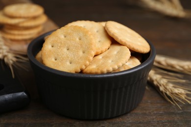 Photo of Tasty salty crackers and wheat spikes on wooden table, closeup