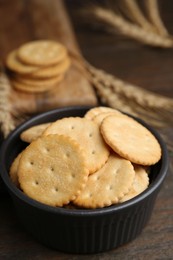 Photo of Tasty salty crackers and wheat spikes on wooden table, closeup