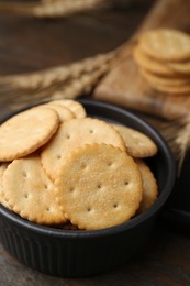 Photo of Tasty salty crackers and wheat spikes on wooden table, closeup