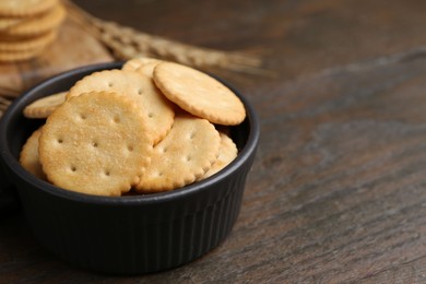 Photo of Tasty salty crackers and wheat spikes on wooden table, closeup. Space for text