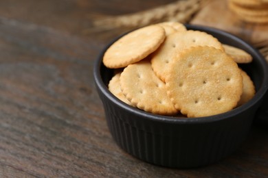 Photo of Tasty salty crackers and wheat spikes on wooden table, closeup. Space for text