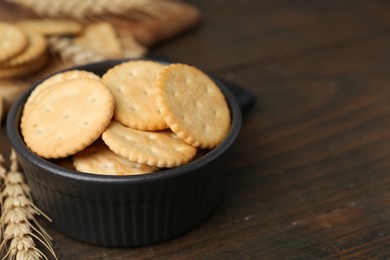 Photo of Tasty salty crackers and wheat spikes on wooden table, closeup. Space for text