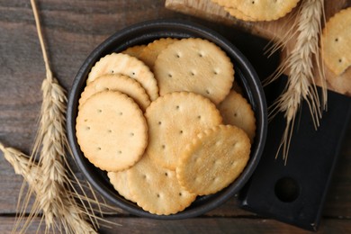 Photo of Tasty salty crackers and wheat spikes on wooden table, flat lay