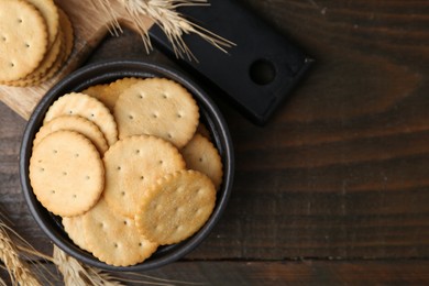 Photo of Tasty salty crackers and wheat spikes on wooden table, flat lay. Space for text