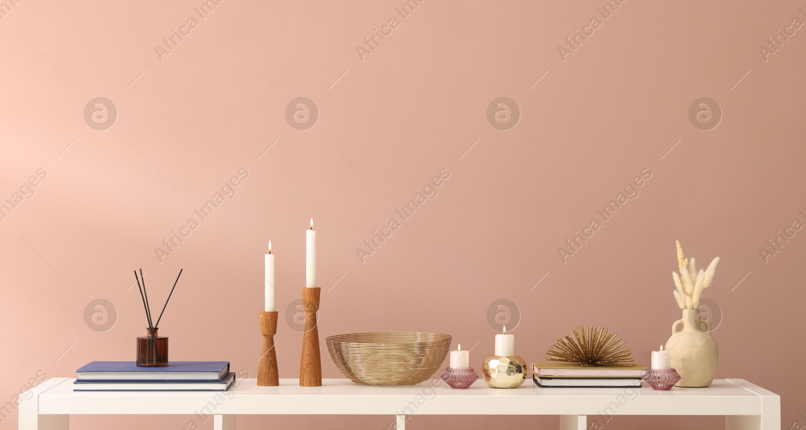 Candlesticks with burning candles and other decor on white wooden table near light brown wall indoors, space for text Photo of Candlesticks with burning candles and other decor on white wooden table near light brown wall indoors, space for text