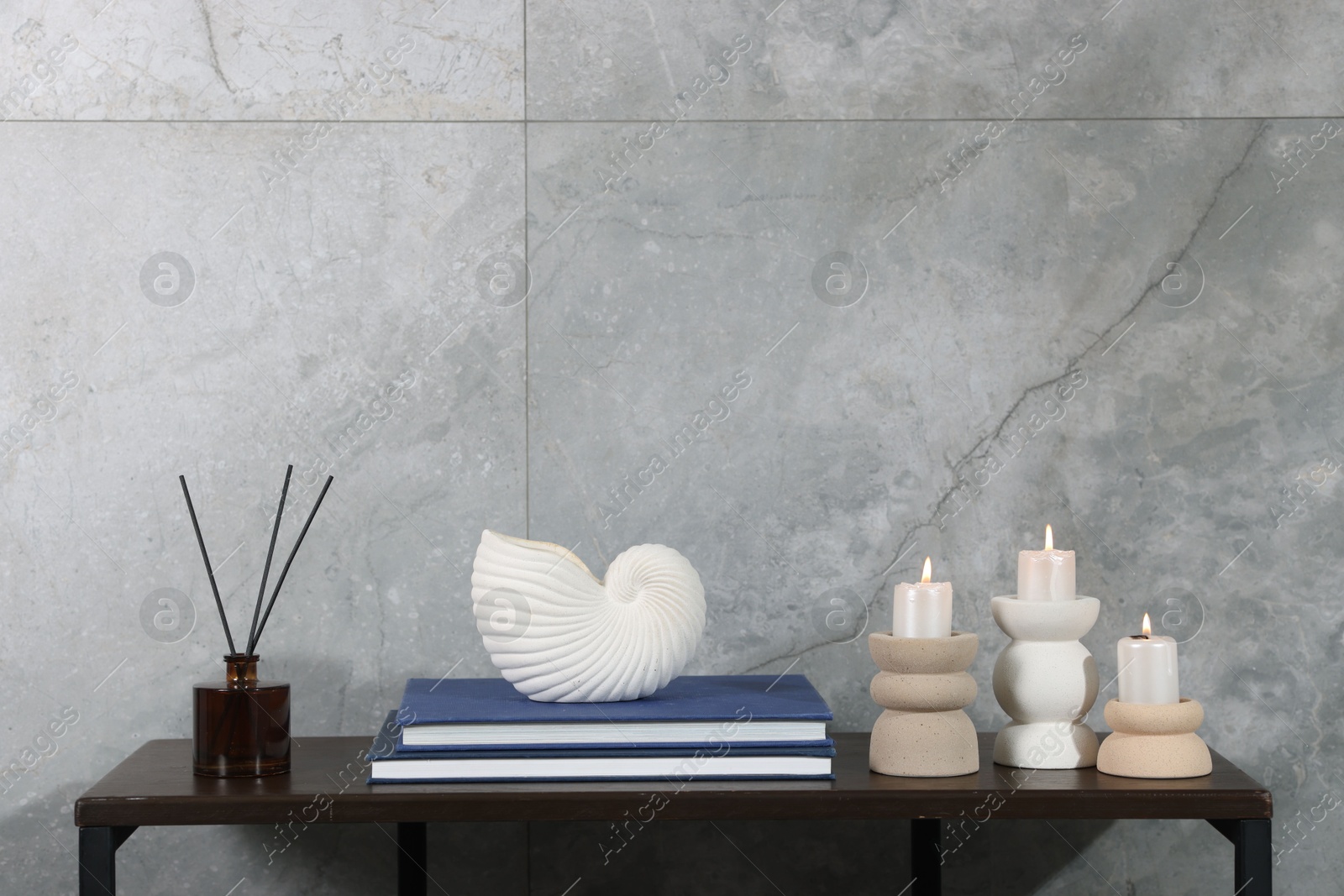 Candlesticks with burning candles and other decor on wooden table near light grey wall indoors, space for text Photo of Candlesticks with burning candles and other decor on wooden table near light grey wall indoors, space for text
