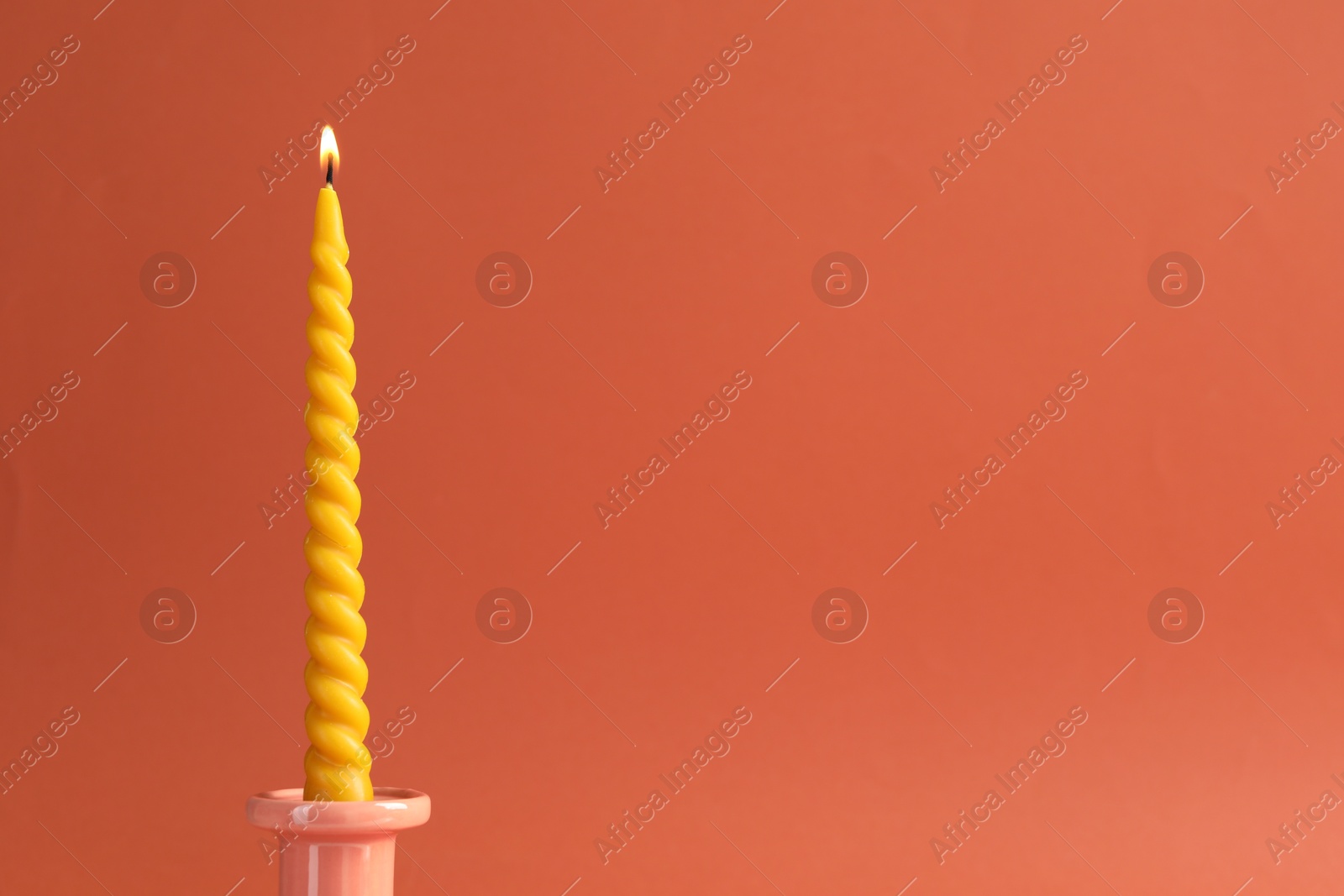 Burning beeswax candle on coral background, closeup. Space for text Photo of Burning beeswax candle on coral background, closeup. Space for text