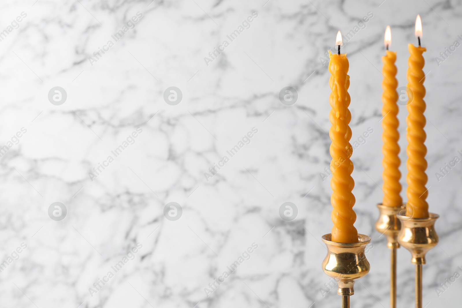 Burning beeswax candles in candlesticks against white marble background, closeup. Space for text Photo of Burning beeswax candles in candlesticks against white marble background, closeup. Space for text