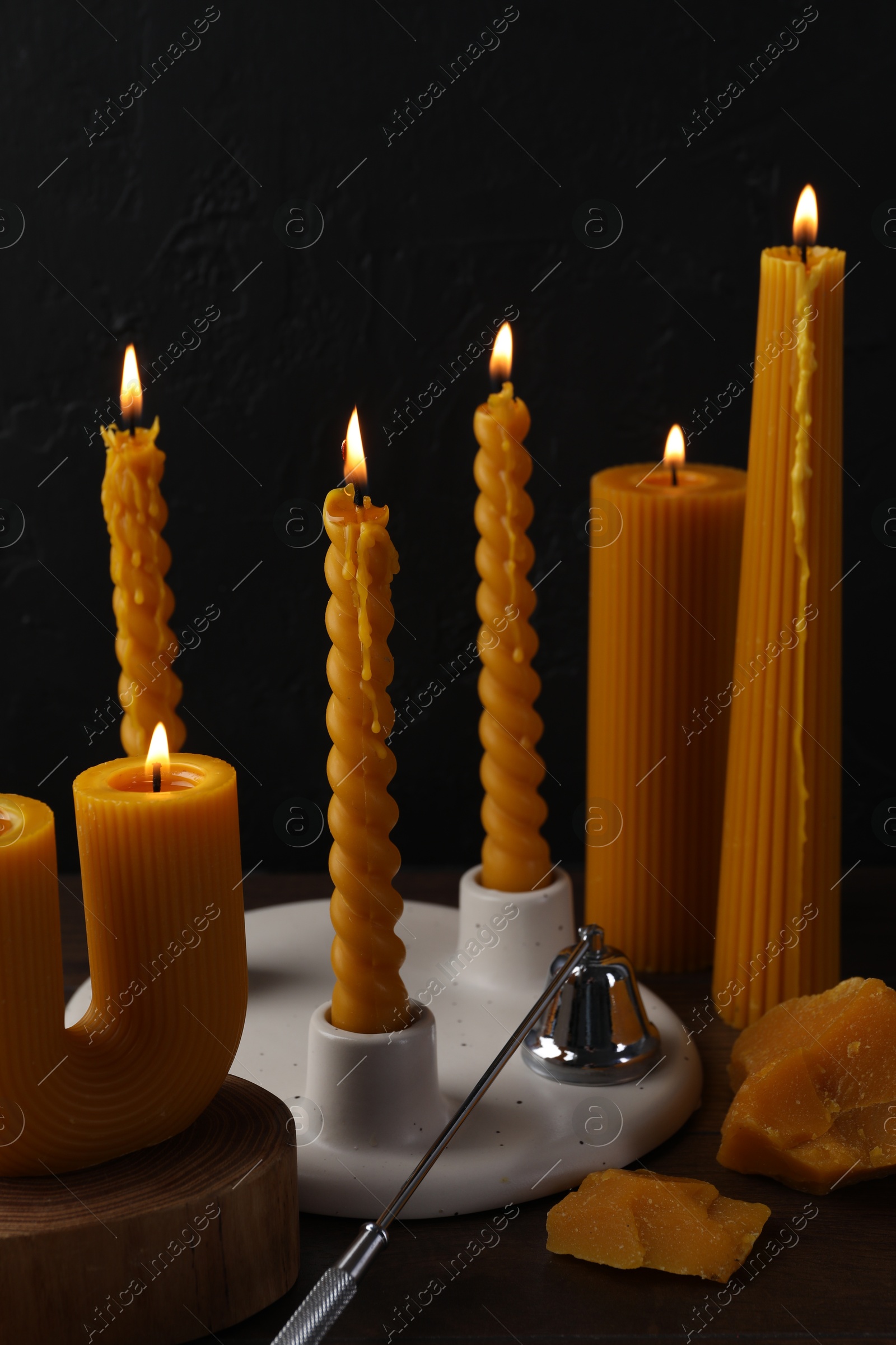 Burning beeswax candles, wax pieces and snuffer on wooden table against black background Photo of Burning beeswax candles, wax pieces and snuffer on wooden table against black background