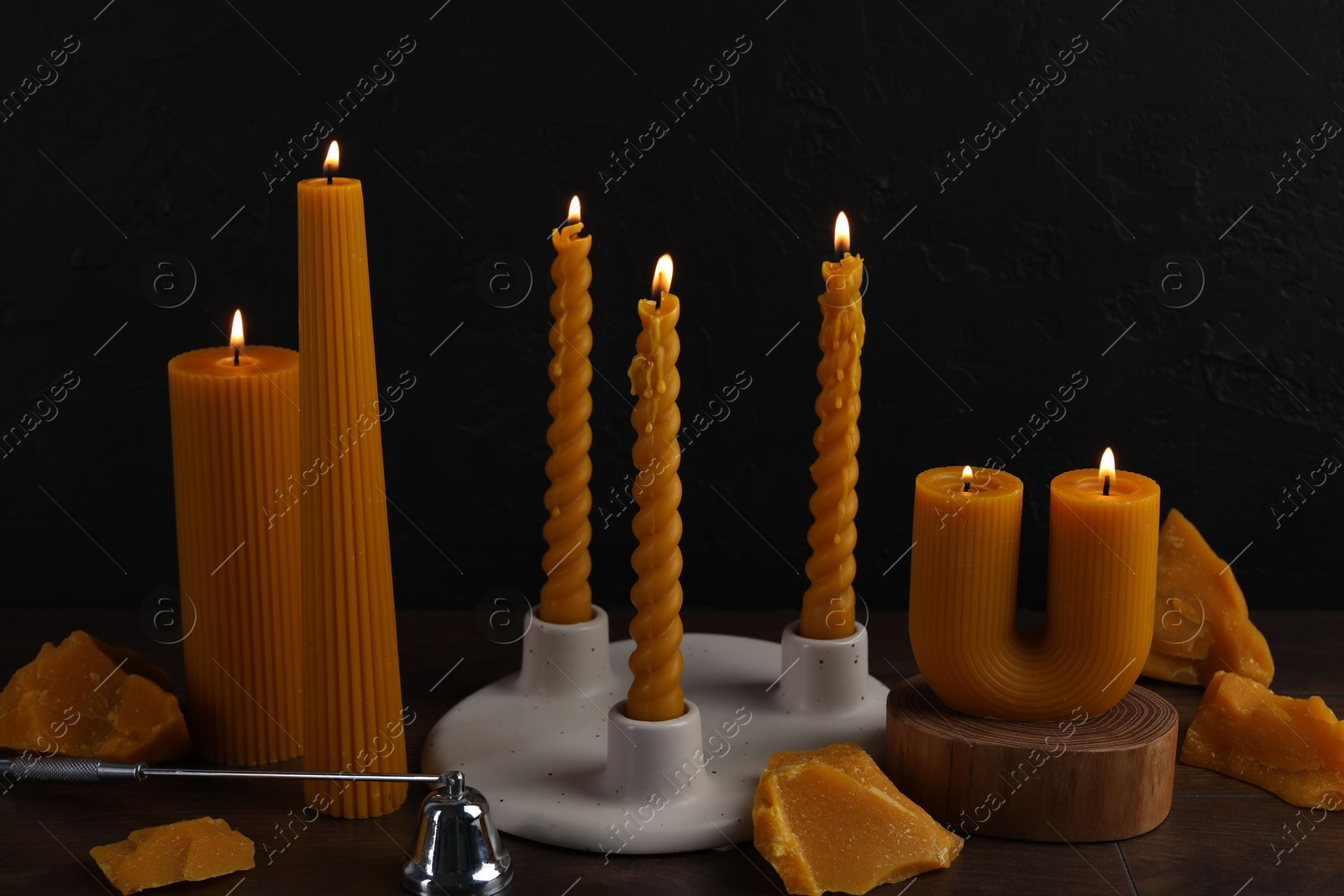 Burning beeswax candles, wax pieces and snuffer on wooden table against black background Photo of Burning beeswax candles, wax pieces and snuffer on wooden table against black background