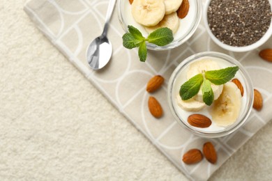 Photo of Delicious dessert with chia seeds, yogurt, banana, almond and mint in glasses on light textured table, top view with space for text. Superfood