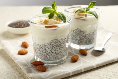 Photo of Delicious dessert with chia seeds, yogurt, banana, almond and mint in glasses on light textured table, closeup. Superfood