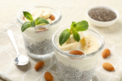 Photo of Delicious dessert with chia seeds, yogurt, banana, almond and mint in glasses on table, closeup. Superfood
