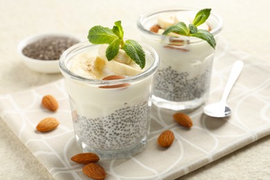 Photo of Delicious dessert with chia seeds, yogurt, banana, almond and mint in glasses on light textured table, closeup. Superfood