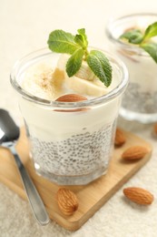 Photo of Delicious dessert with chia seeds, yogurt, banana, almond and mint in glasses on light textured table, closeup. Superfood